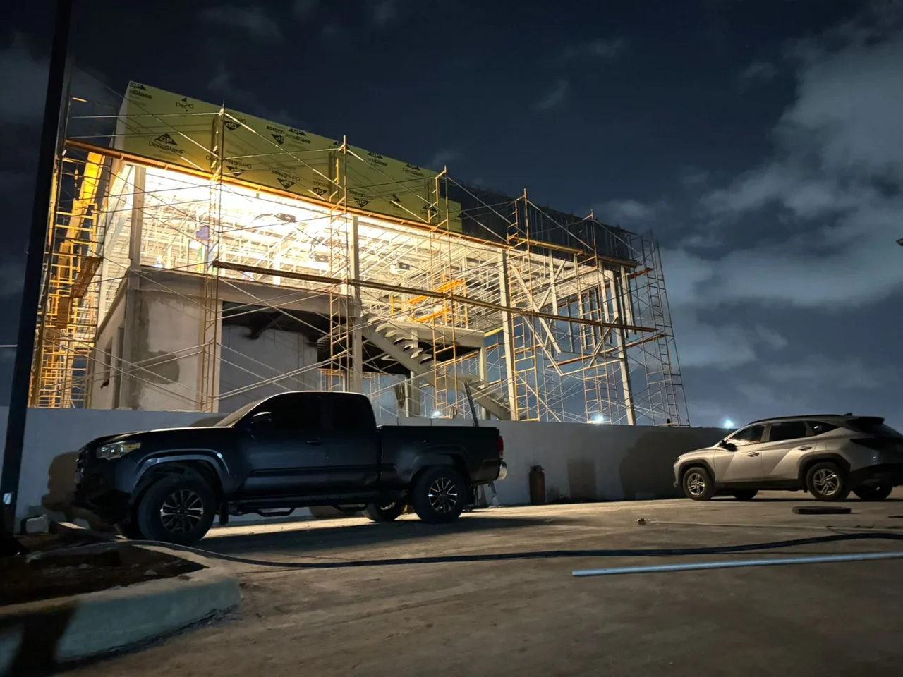 Nighttime exterior of the Shacman dealership under construction, with scaffolding around the building