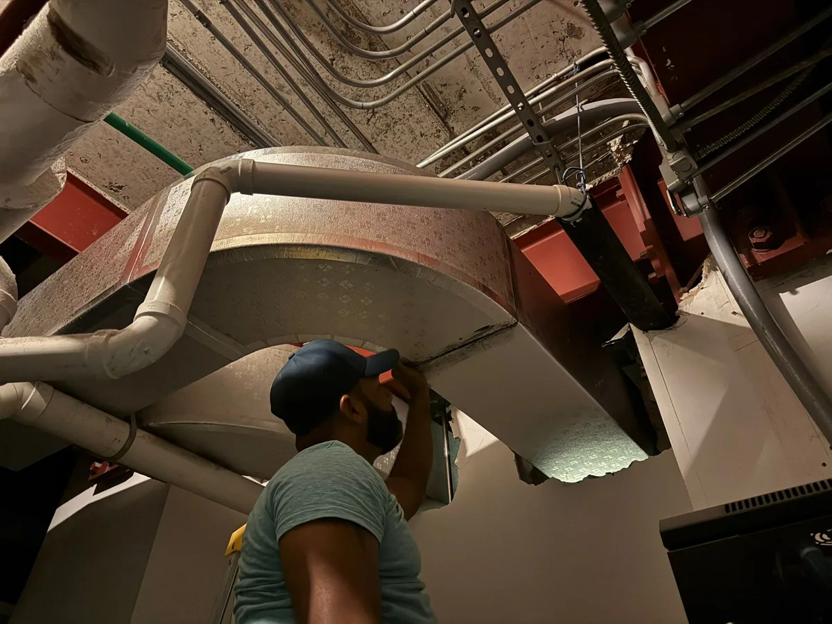 Person working among ducts and piping above an indoor space