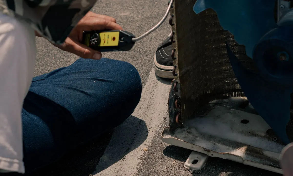 Technician taking a measurement beside an outdoor air-conditioning unit